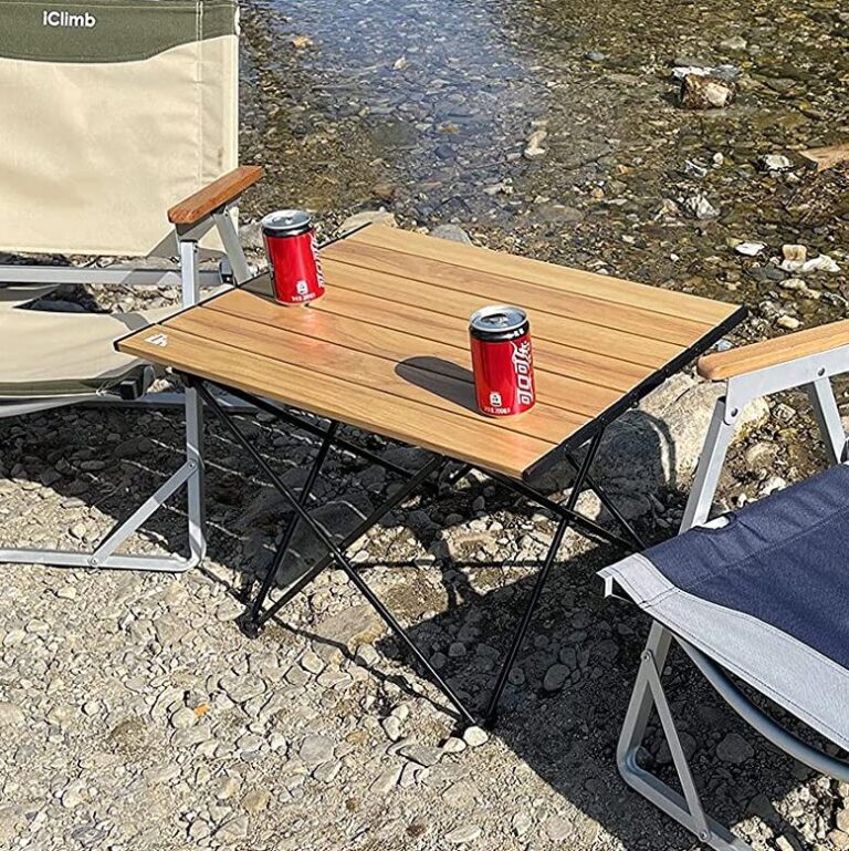 A portable camping table being used to keep a drink and a book off of the ground.