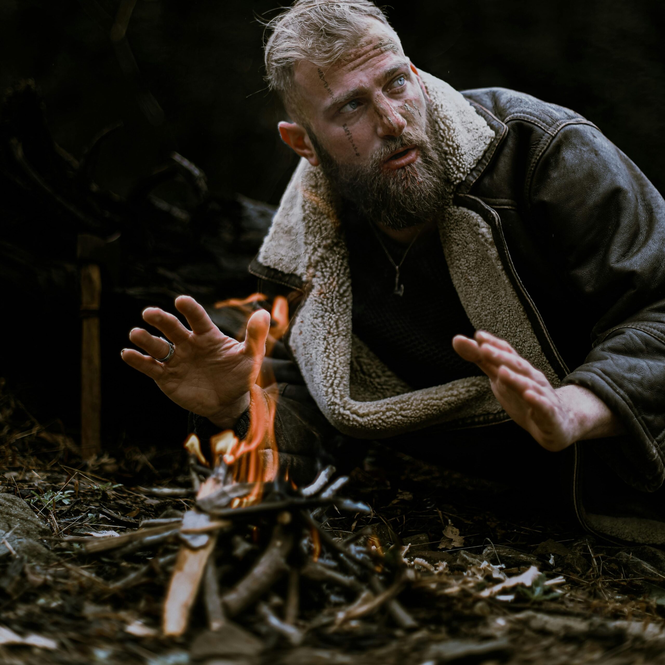 A man huddled by the fire looking worried 